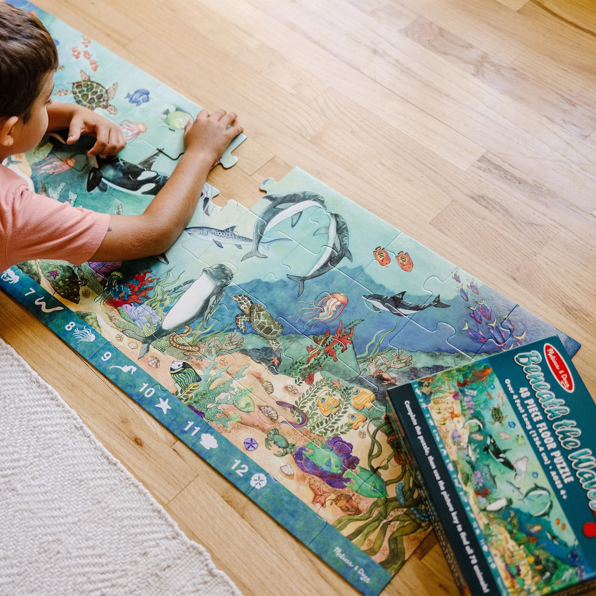 A kid playing with The Melissa & Doug Search and Find Beneath the Waves Floor Puzzle (48 pcs, over 4 feet long)